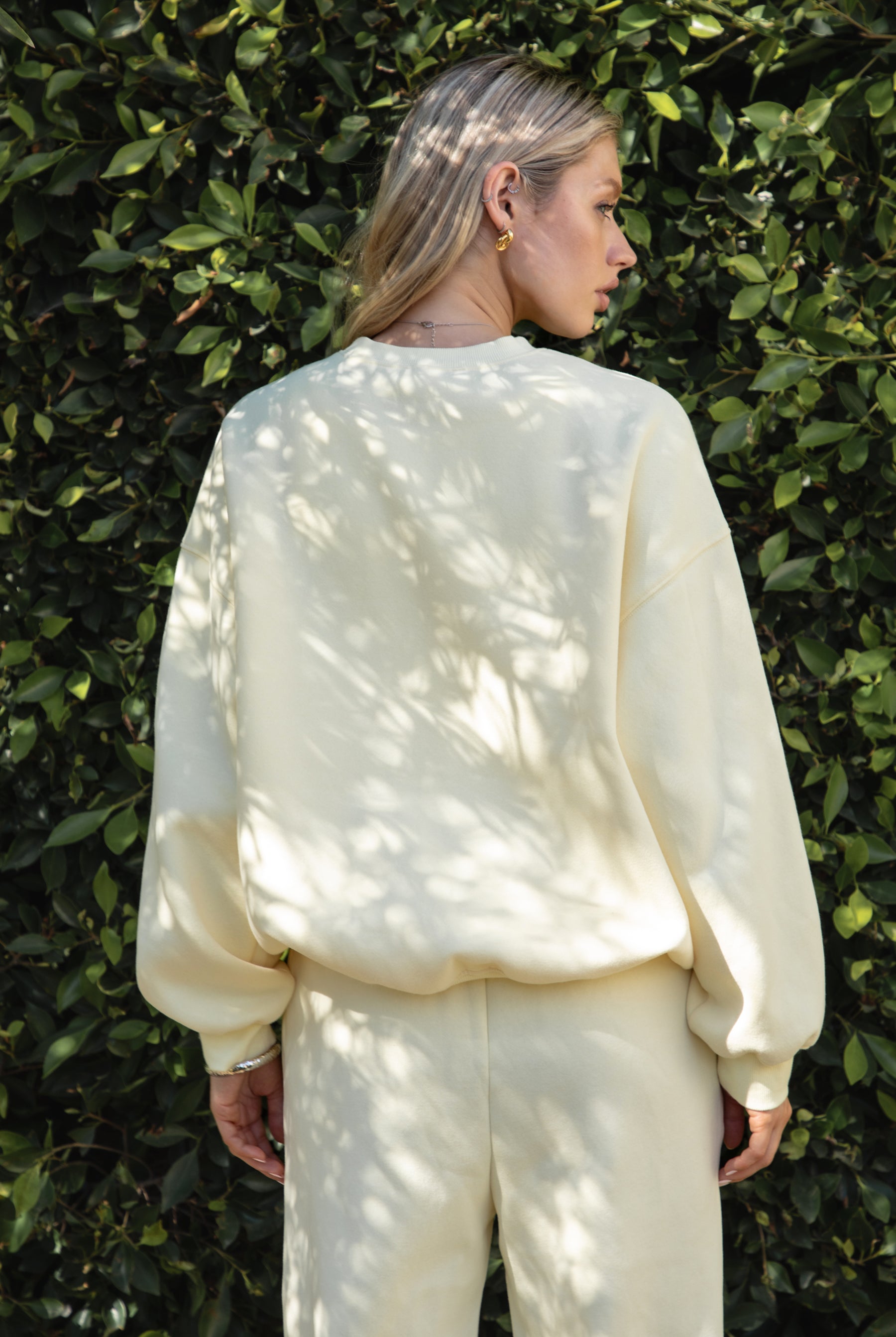 Woman wearing a yellow colored outfit standing against a green leafy background