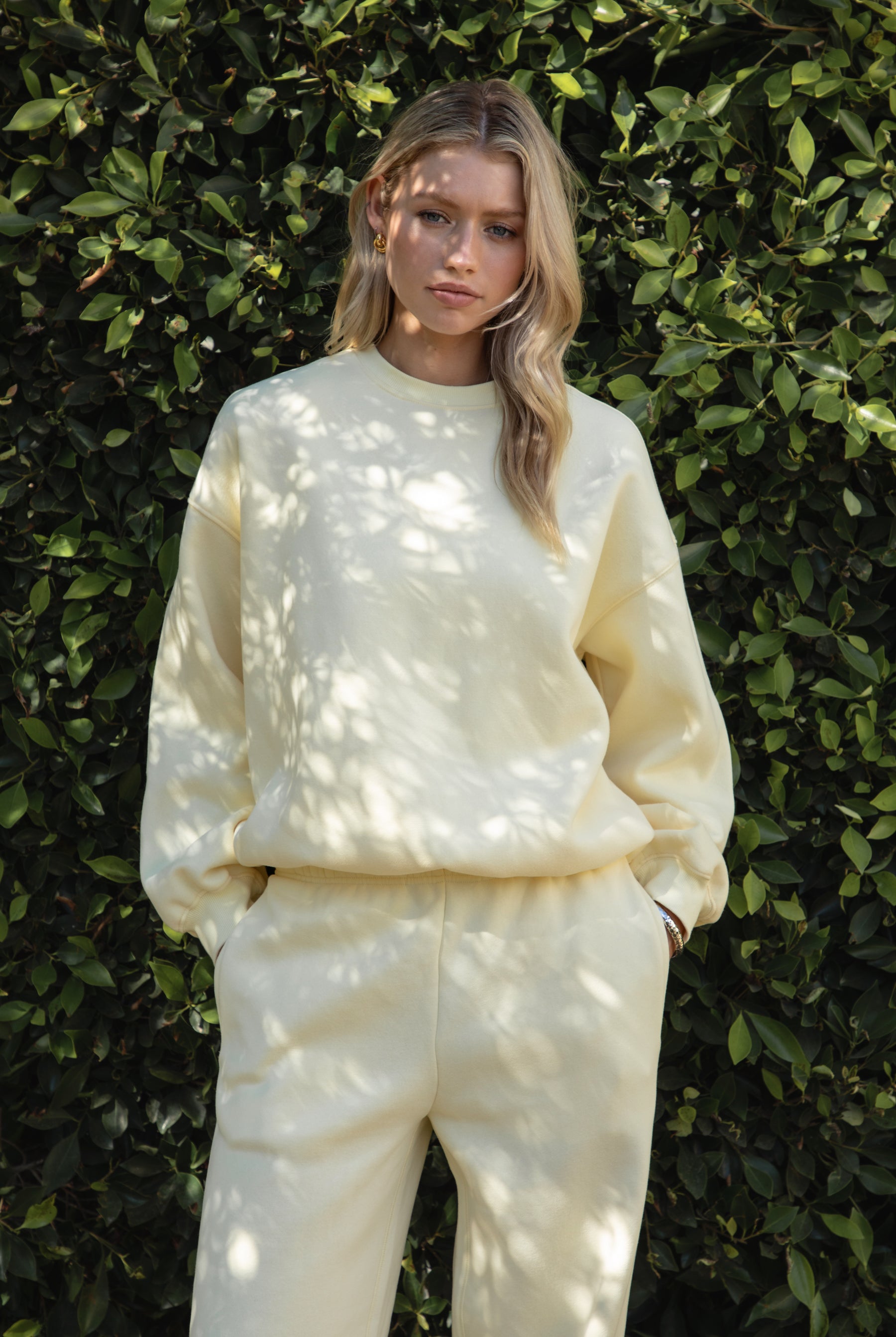 Woman wearing a yellow colored outfit standing against a green leafy background
