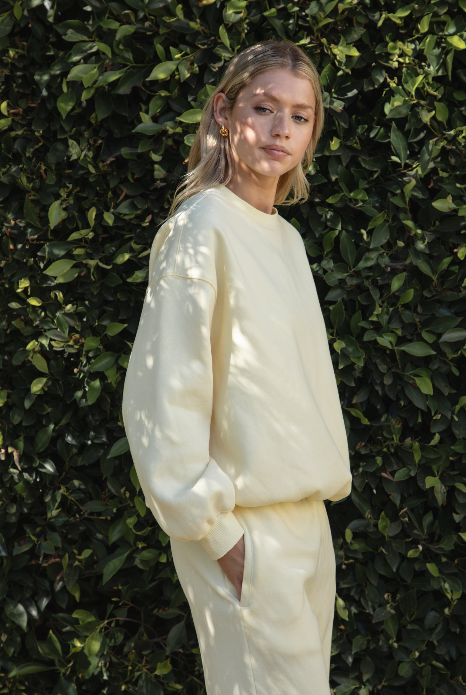 Woman wearing a yellow colored outfit standing against a green leafy background