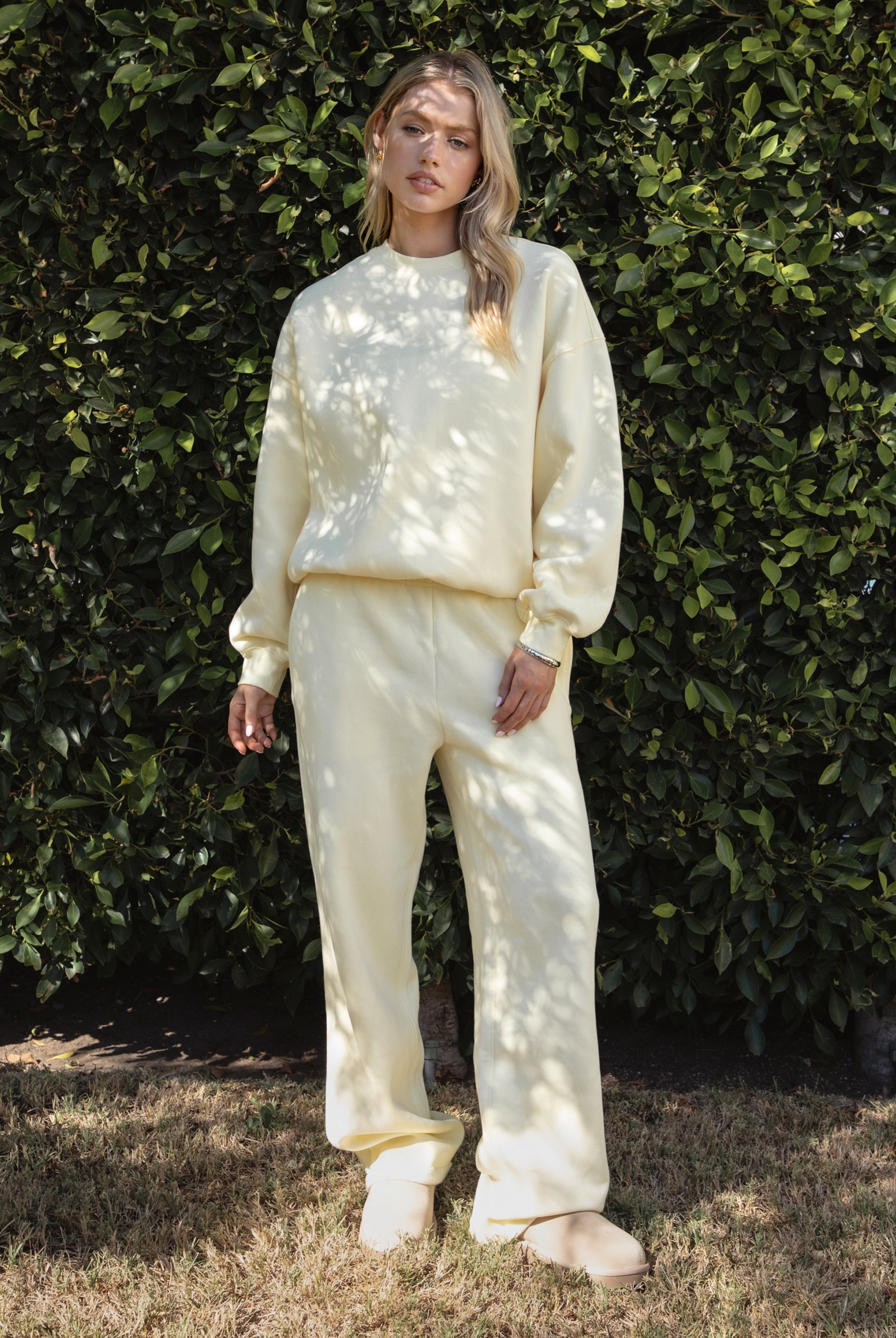 Woman wearing a yellow colored outfit standing against a green leafy background