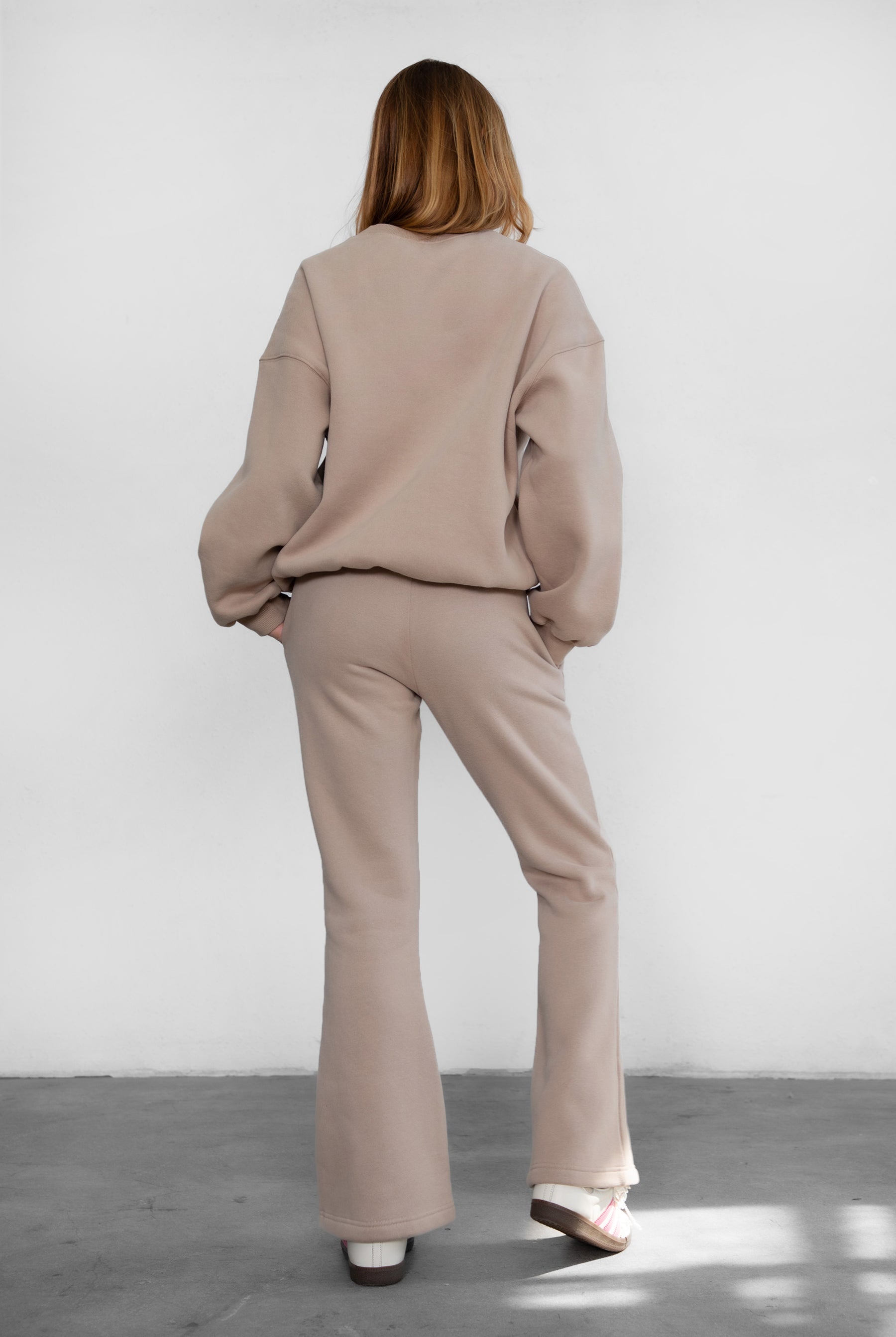 Person wearing a beige outfit standing against a white wall.