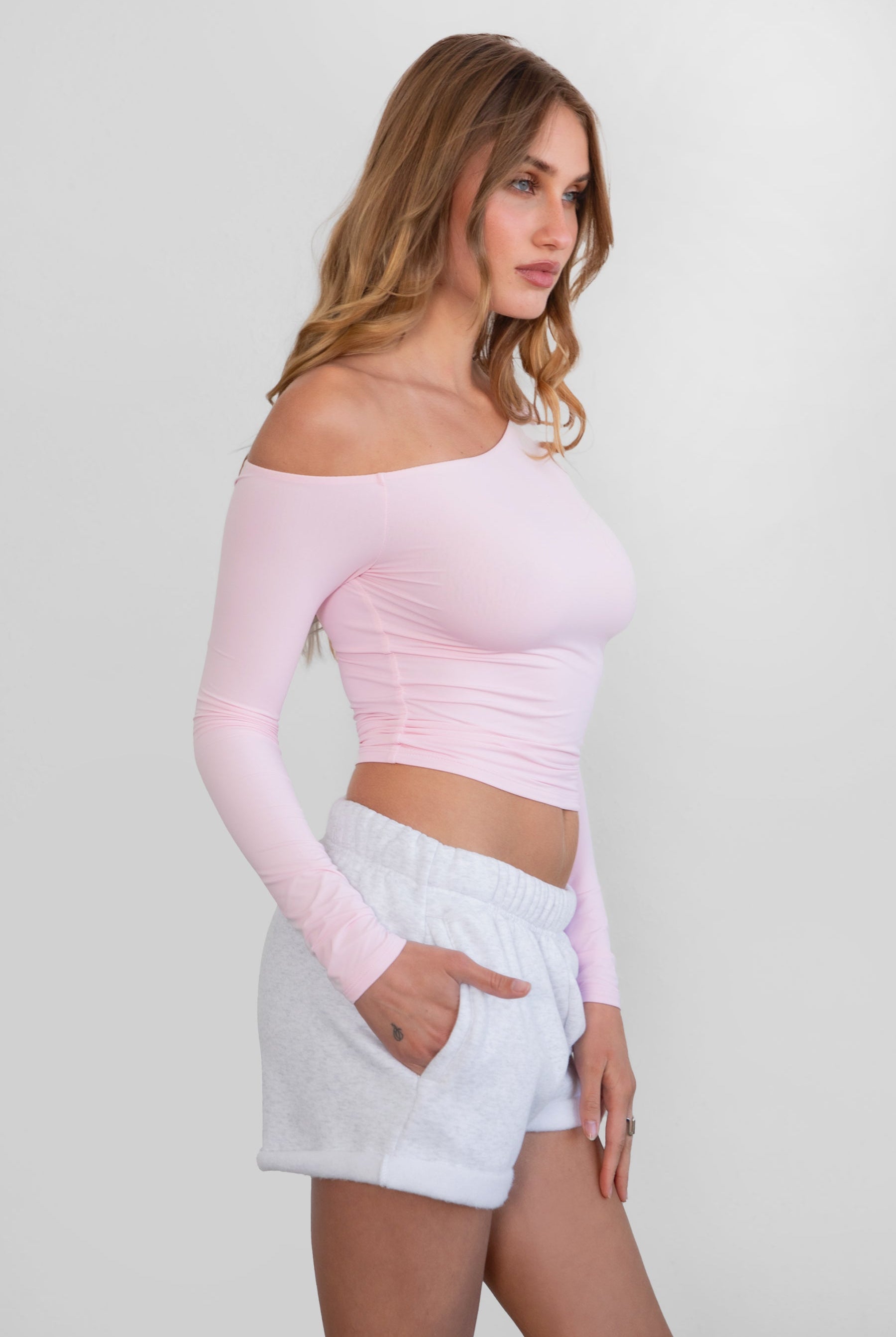 Woman wearing TIC TOC TH30538 AUDREE lightweight one-shoulder long sleeve top in slim fit stretch fabric in color blush paired with ash fleece shorts.