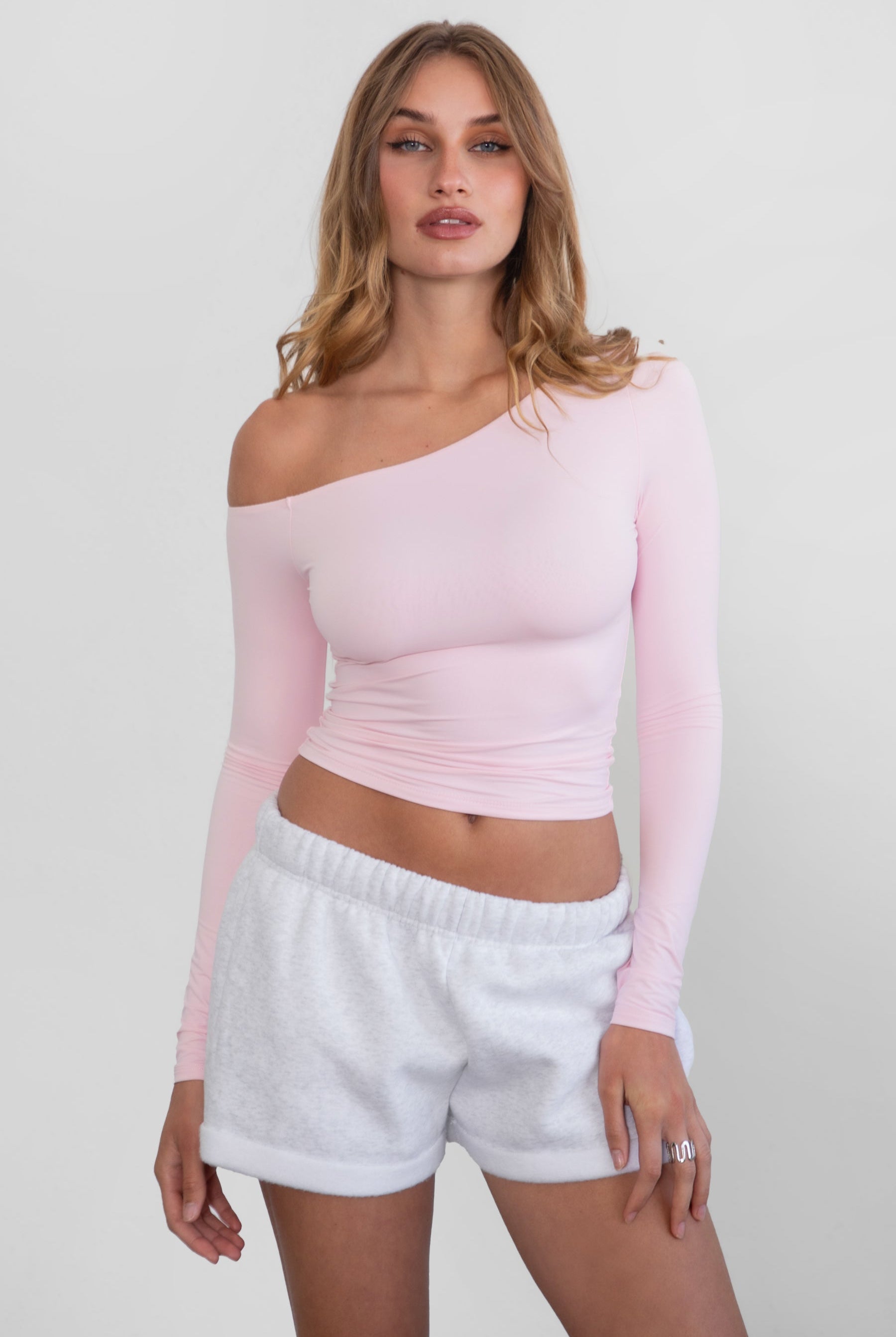 Woman wearing TIC TOC TH30538 AUDREE lightweight one-shoulder long sleeve top in slim fit stretch fabric in color blush paired with ash fleece shorts.