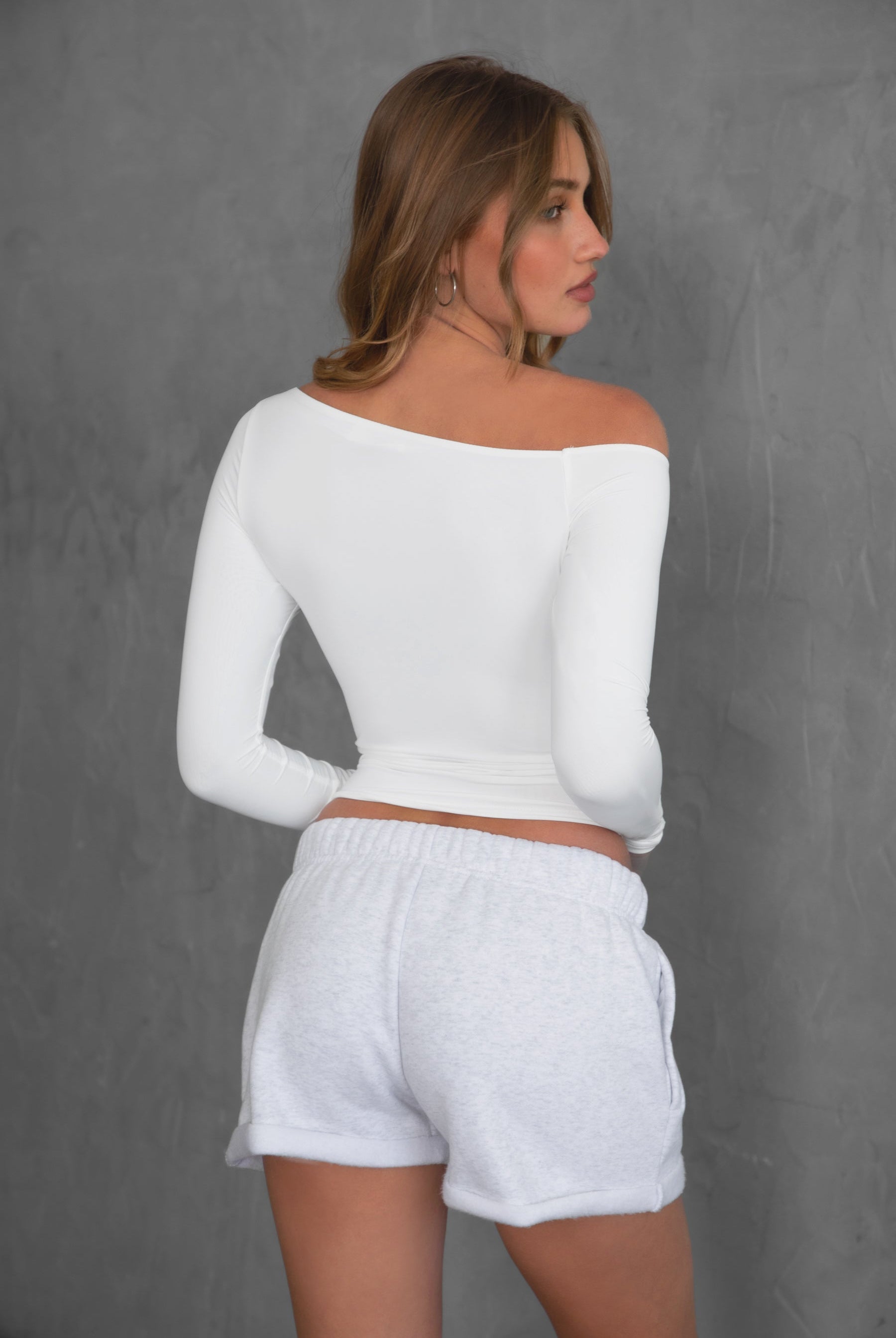 Woman wearing TIC TOC TH30538 AUDREE lightweight one-shoulder long sleeve top in slim fit stretch fabric in color white paired with fleece shorts.