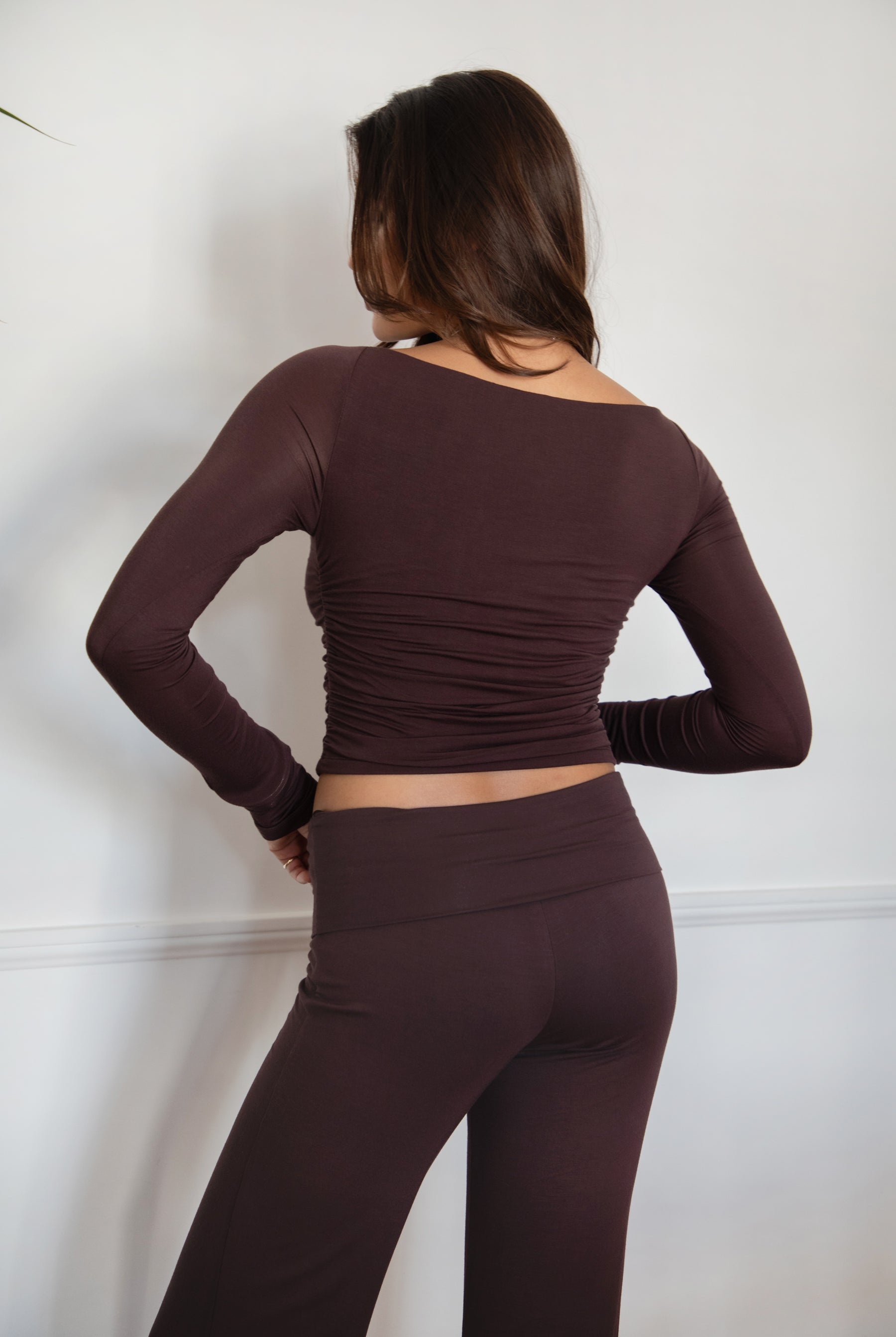Woman wearing the TIC TOC TH30643 JOLINA brown core basic long sleeve top featuring high boat neckline, and ruched detailing along the bodice with matching bottoms in an indoor setting.