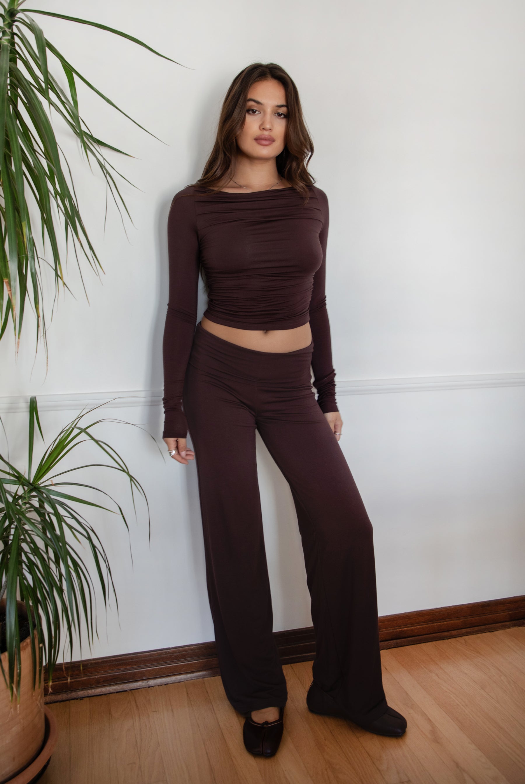 Woman wearing the TIC TOC TH30643 JOLINA brown core basic long sleeve top featuring high boat neckline, and ruched detailing along the bodice with matching bottoms in an indoor setting.