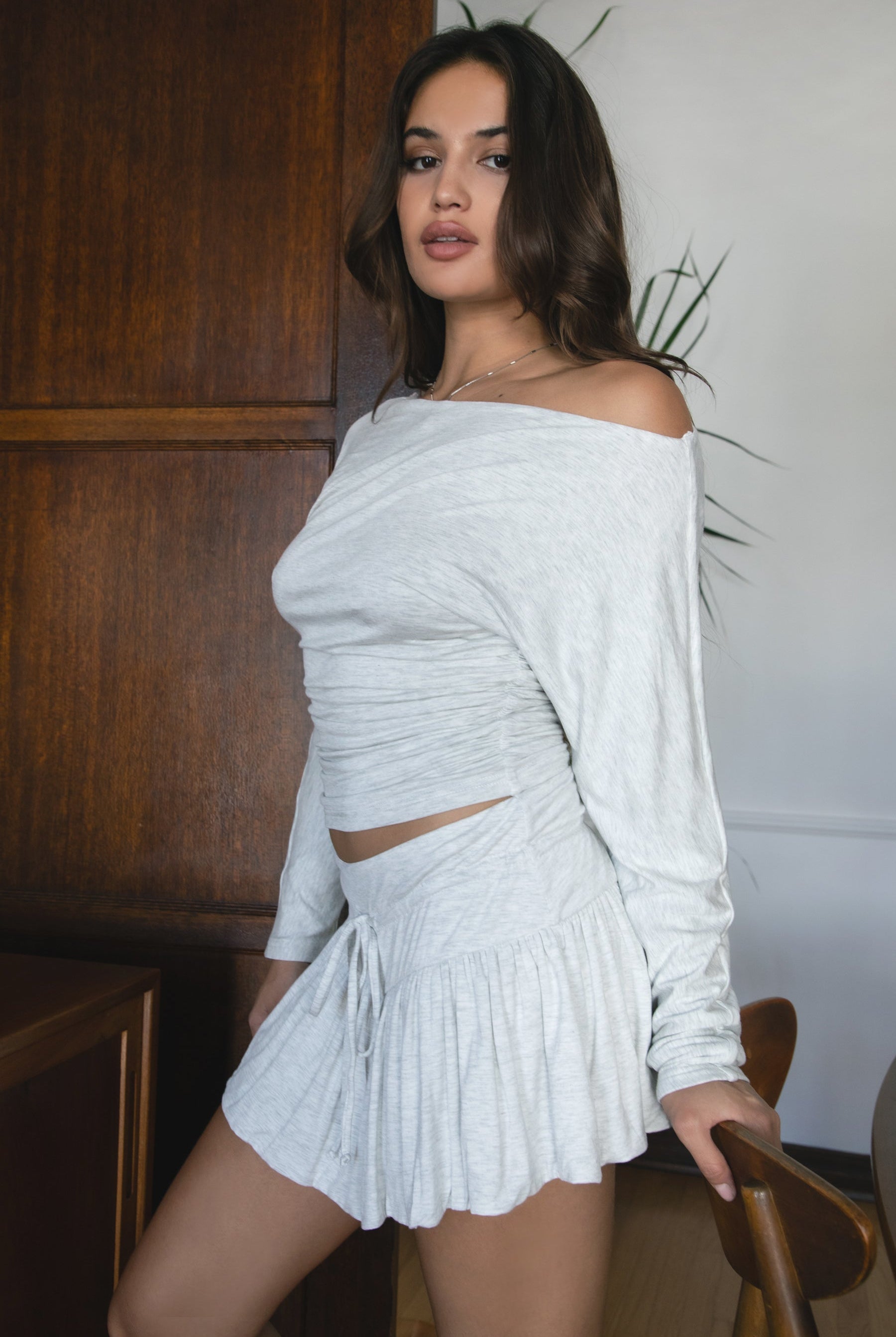 Woman wearing the TIC TOC TH31856BA SORA heather white asymmetric off-the-shoulder long sleeve top featuring a slouchy cropped fit, wide boat neckline, and soft stretch fabric with matching skirt.