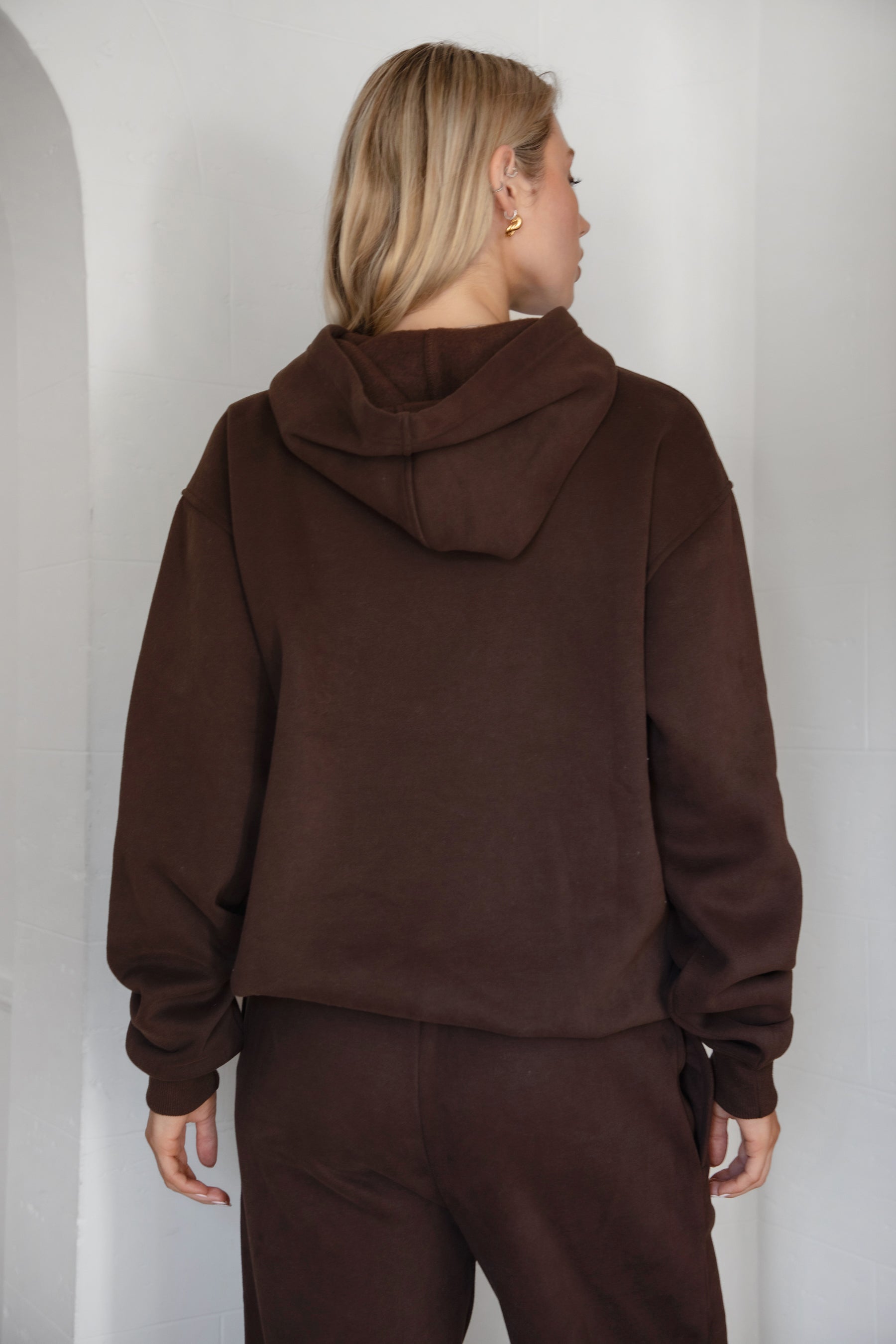Woman wearing the TIC TOC TJ31007 DAMI dark brown cloud fleece oversized hoodie featuring a dropped shoulder design, kangaroo pocket, and ribbed cuffs with matching bottoms.
