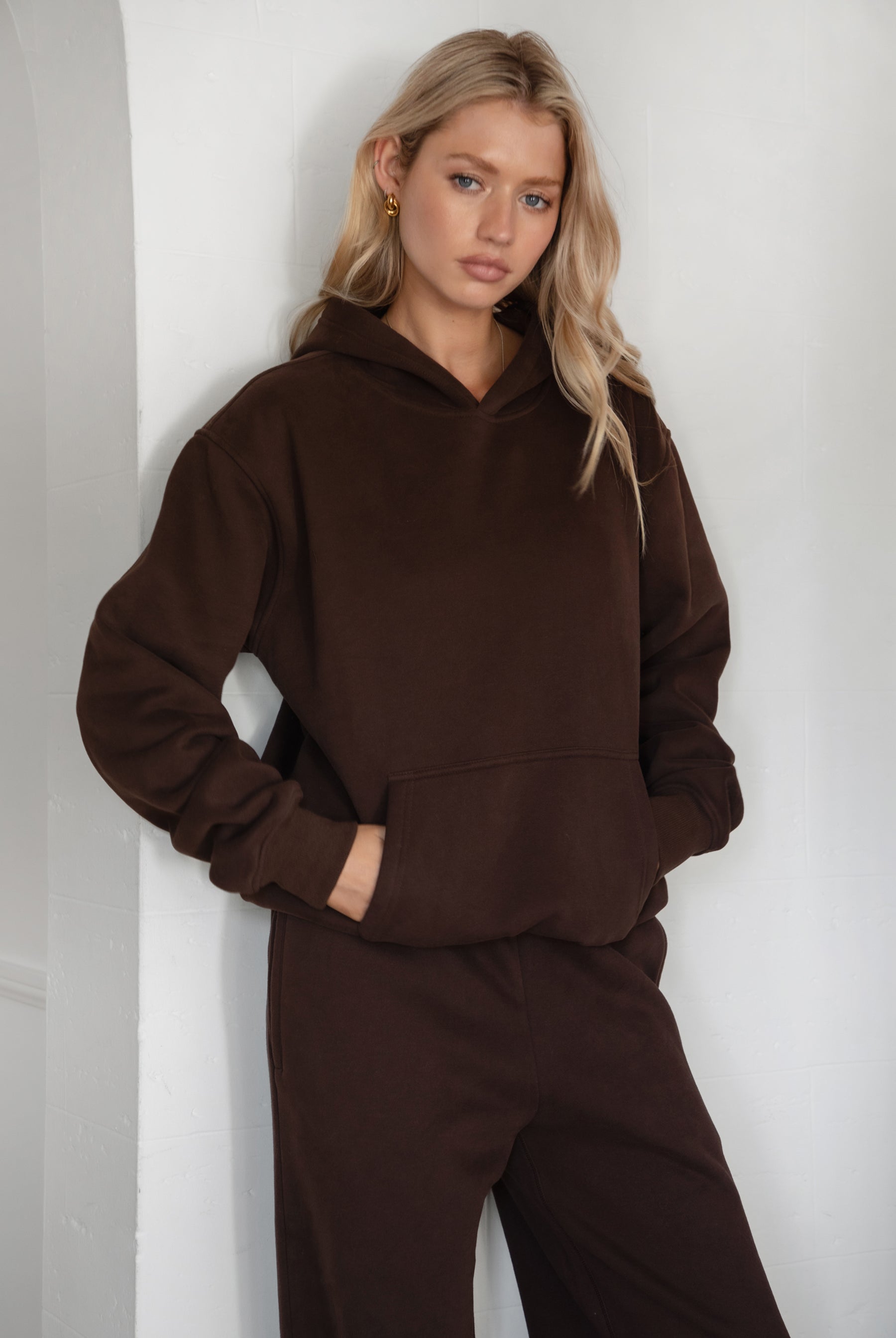 Woman wearing the TIC TOC TJ31007 DAMI dark brown cloud fleece oversized hoodie featuring a dropped shoulder design, kangaroo pocket, and ribbed cuffs with matching bottoms.