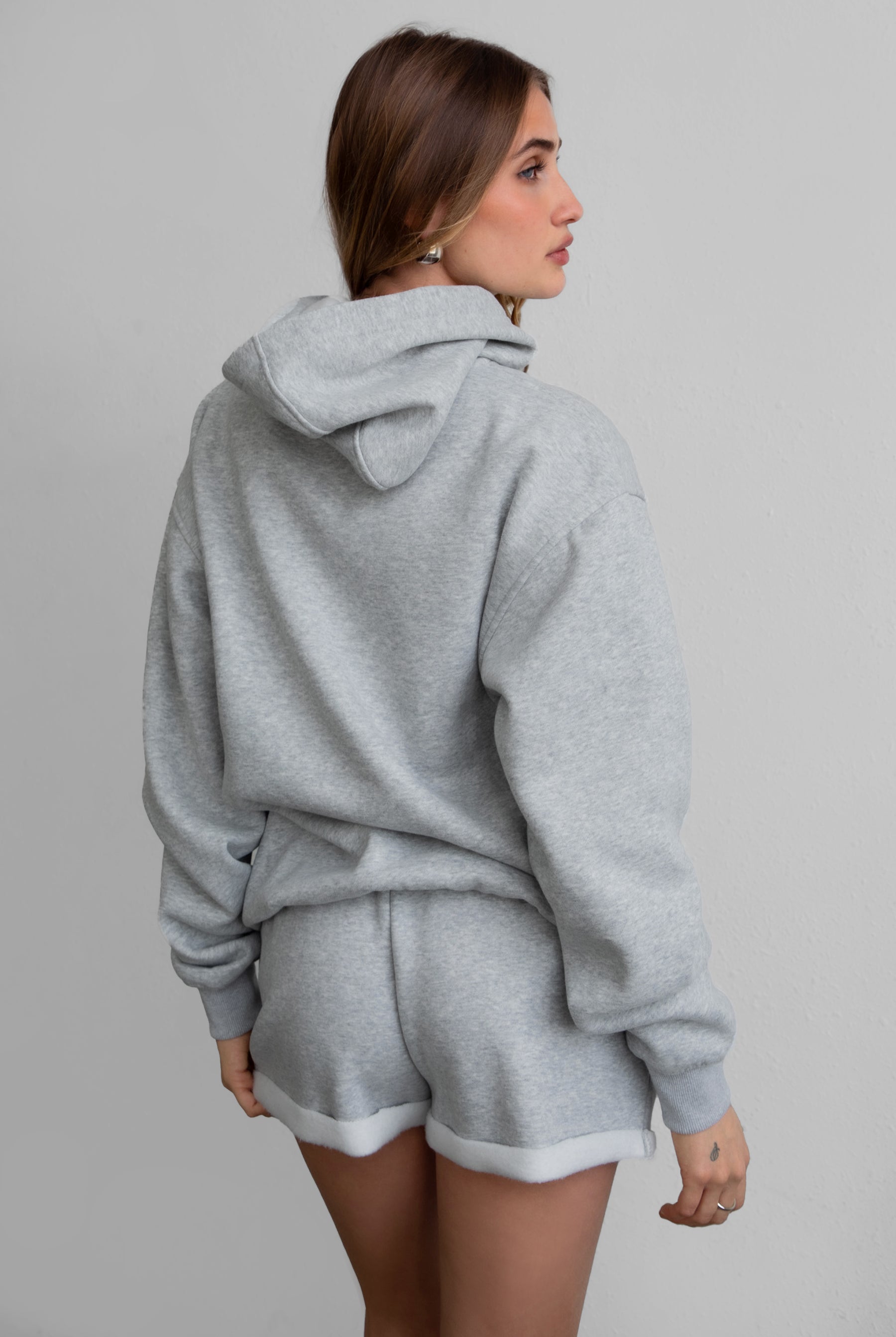 Woman wearing the TIC TOC TJ31007 DAMI heather grey cloud fleece oversized hoodie featuring a dropped shoulder design, kangaroo pocket, and ribbed cuffs with matching bottoms.