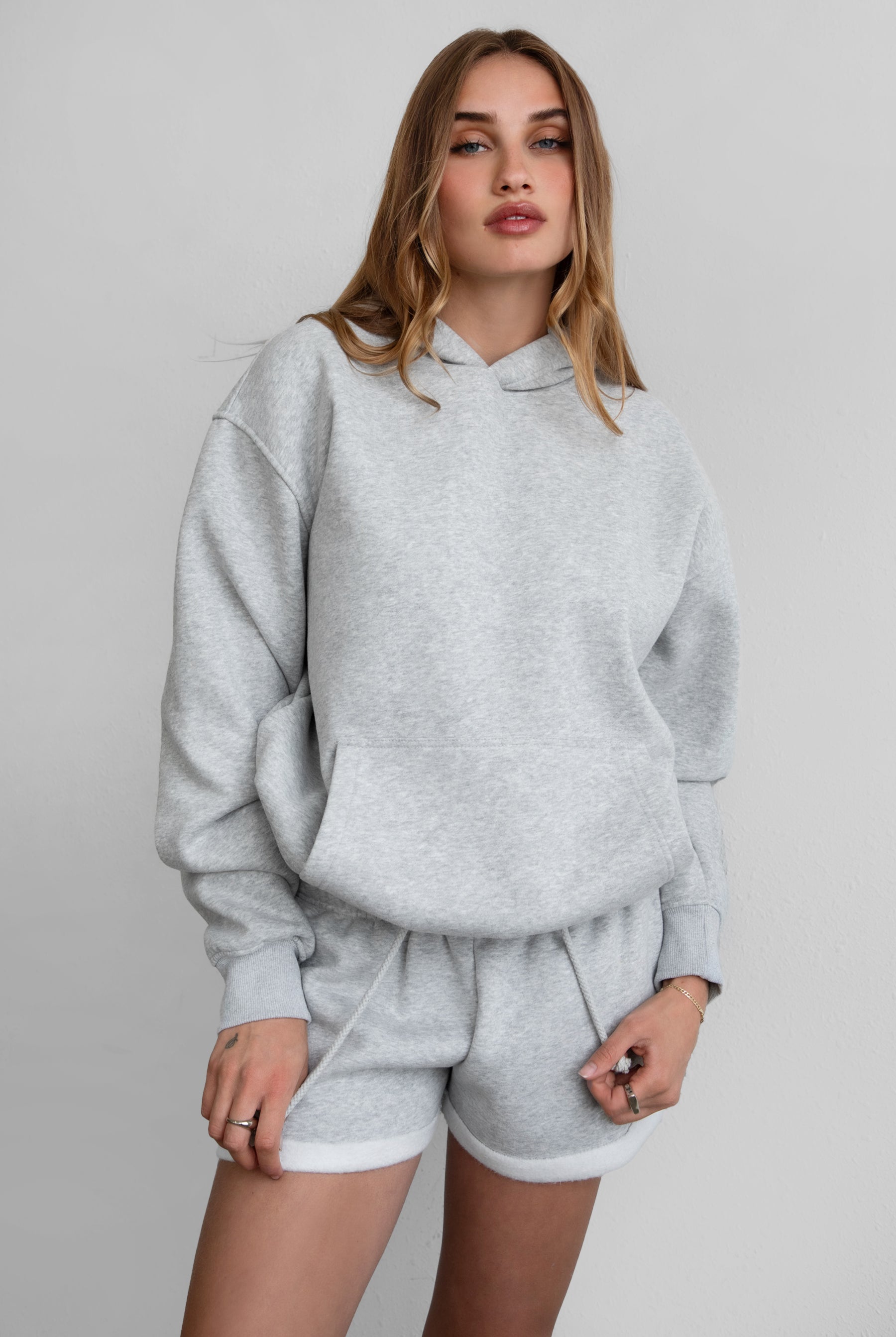 Woman wearing the TIC TOC TJ31007 DAMI heather grey cloud fleece oversized hoodie featuring a dropped shoulder design, kangaroo pocket, and ribbed cuffs with matching bottoms.