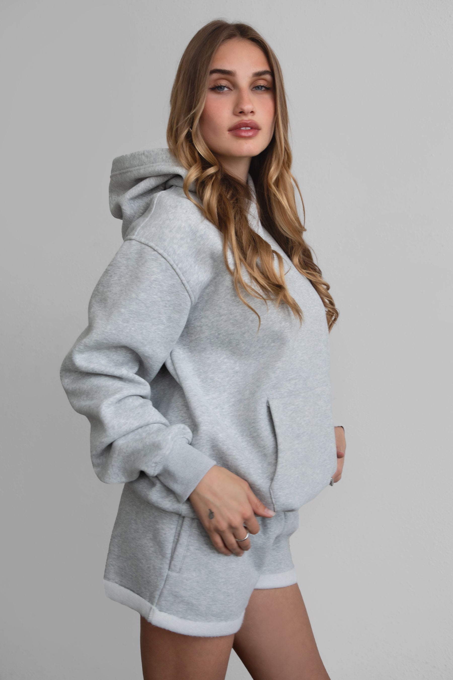 Woman wearing the TIC TOC TJ31007 DAMI heather grey cloud fleece oversized hoodie featuring a dropped shoulder design, kangaroo pocket, and ribbed cuffs with matching bottoms.