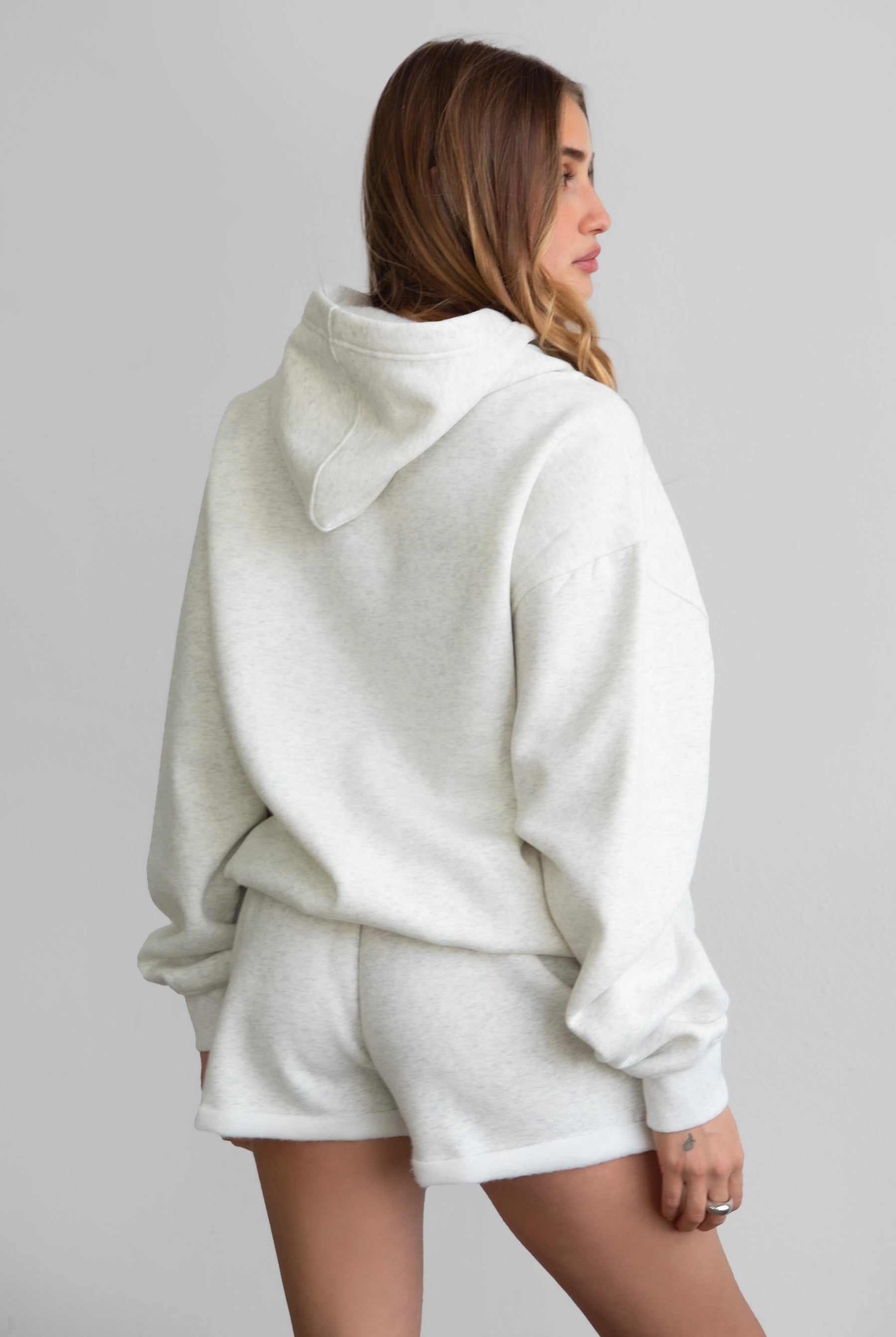 Woman wearing the TIC TOC TJ31007 DAMI heather white cloud fleece oversized hoodie featuring a dropped shoulder design, kangaroo pocket, and ribbed cuffs with matching bottoms.