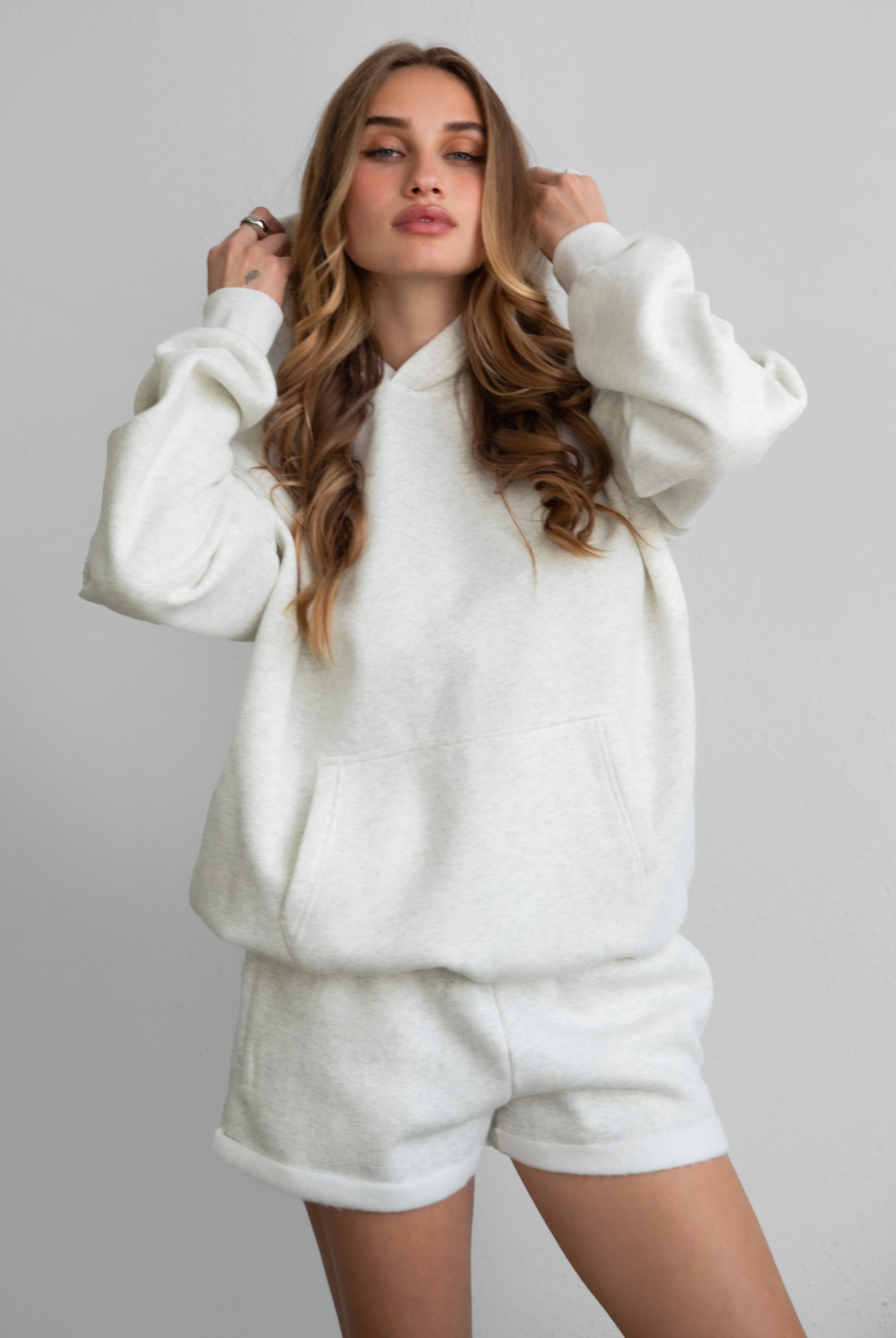 Woman wearing the TIC TOC TJ31007 DAMI heather white cloud fleece oversized hoodie featuring a dropped shoulder design, kangaroo pocket, and ribbed cuffs with matching bottoms.