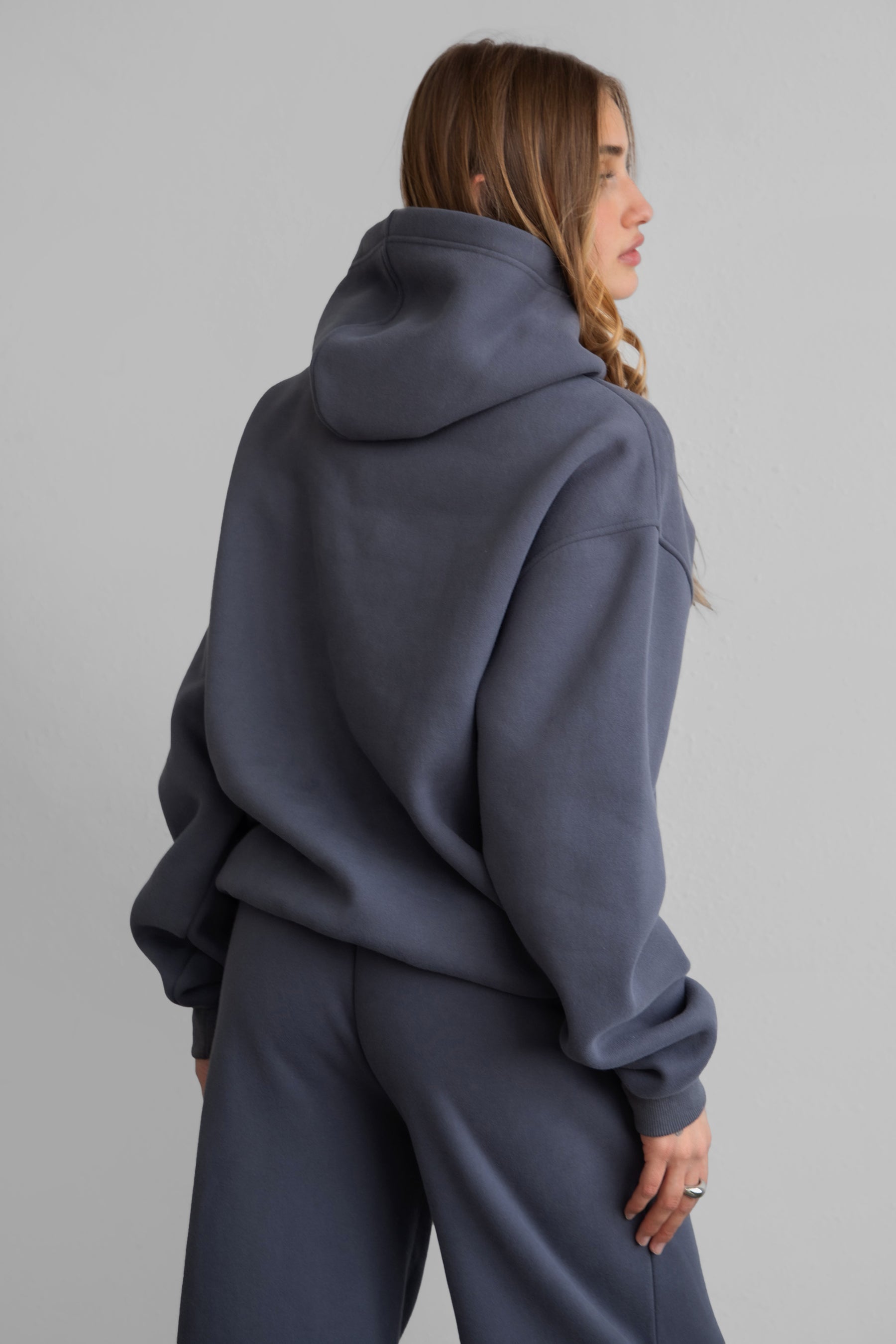 Woman wearing the TIC TOC TJ31007 DAMI steel grey cloud fleece oversized hoodie featuring a dropped shoulder design, kangaroo pocket, and ribbed cuffs with matching bottoms.