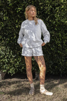 Woman wearing the TIC TOC TJ31656 LANI ash cloud fleece crew neck pullover sweatshirt featuring dropped shoulders, ribbed trim, and cozy fleece fabric with the matching bottoms  against a green leafy background.