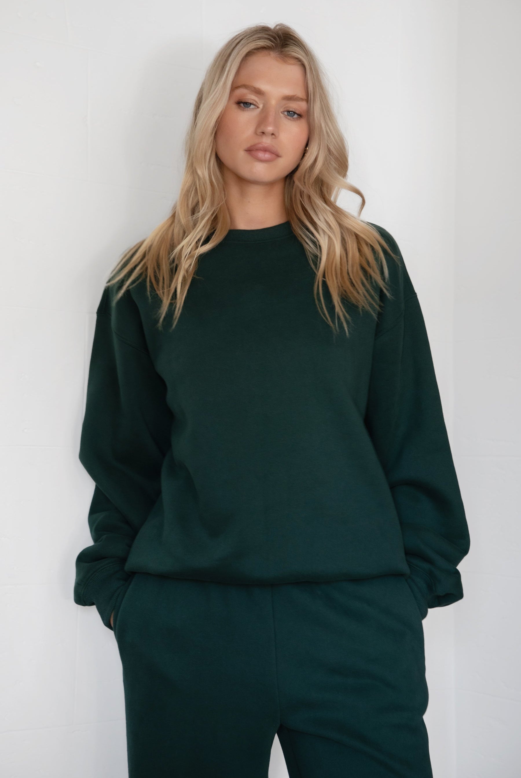 Woman wearing the TIC TOC TJ31656 LANI forrest green cloud fleece crew neck pullover sweatshirt featuring dropped shoulders, ribbed trim, and cozy fleece fabric with the matching bottoms .