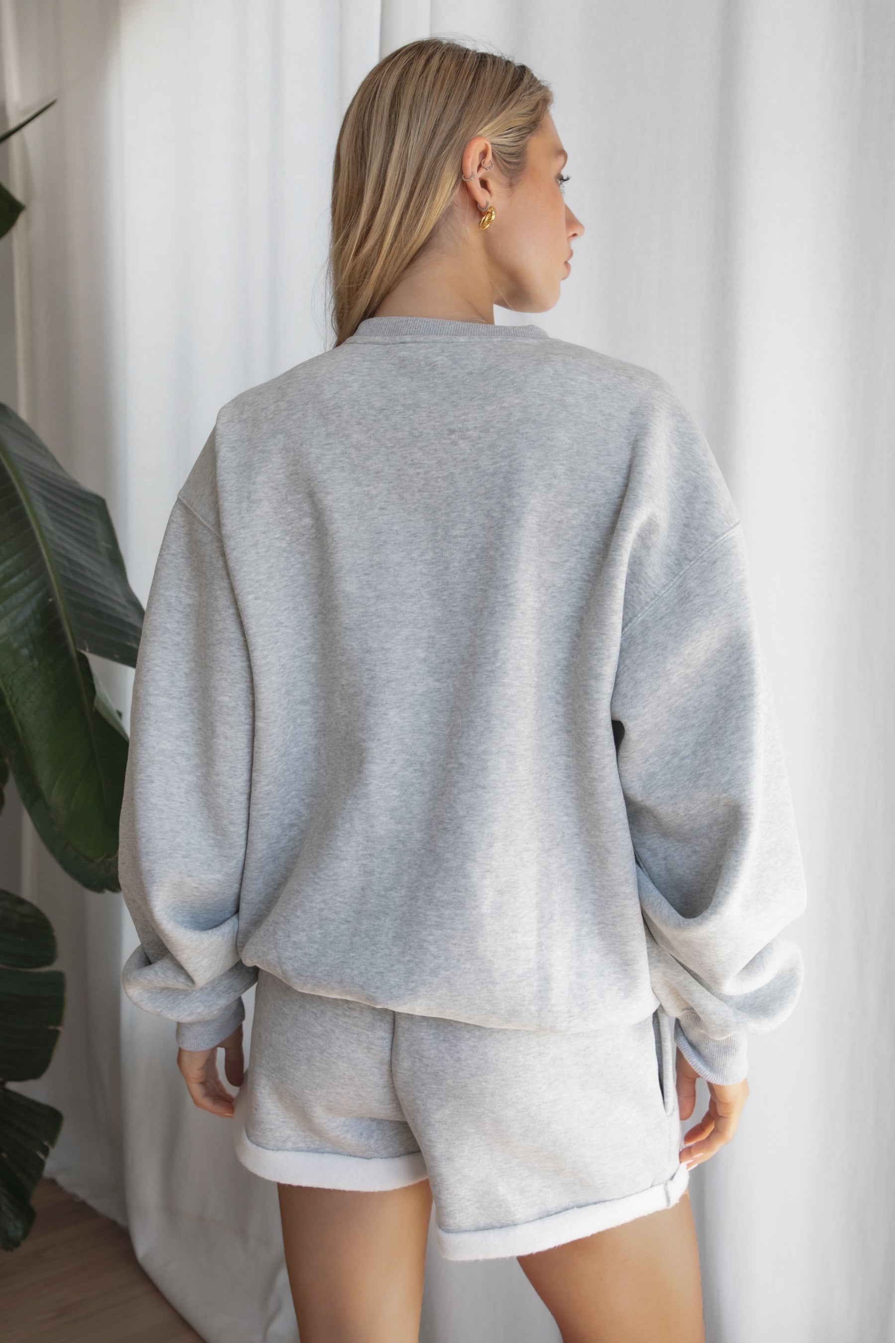 Woman wearing the TIC TOC TJ31656 LANI heather grey cloud fleece crew neck pullover sweatshirt featuring dropped shoulders, ribbed trim, and cozy fleece fabric with the matching bottoms .