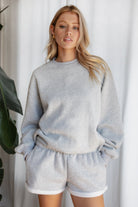 Woman wearing the TIC TOC TJ31656 LANI heather grey cloud fleece crew neck pullover sweatshirt featuring dropped shoulders, ribbed trim, and cozy fleece fabric with the matching bottoms .