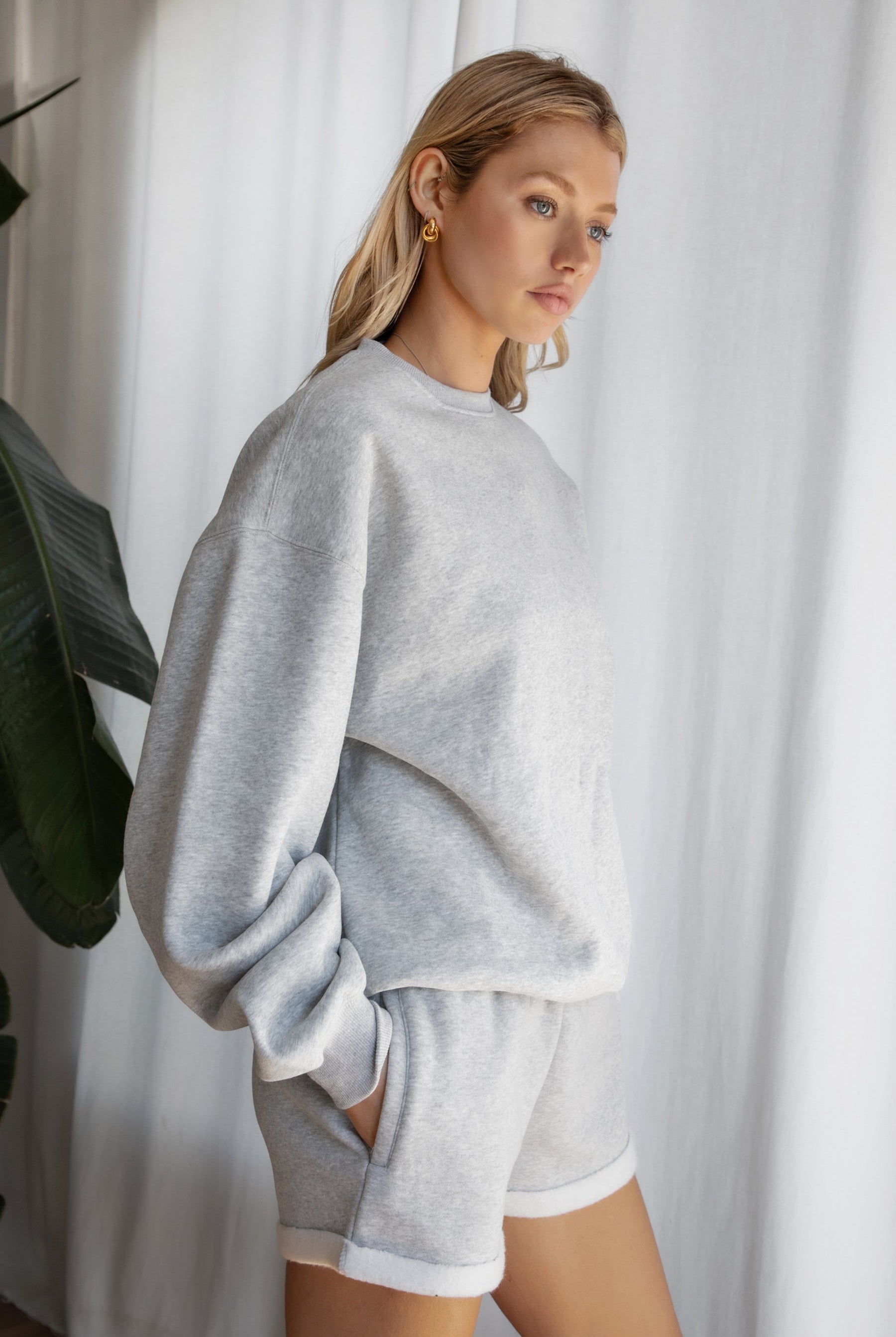 Woman wearing the TIC TOC TJ31656 LANI heather grey cloud fleece crew neck pullover sweatshirt featuring dropped shoulders, ribbed trim, and cozy fleece fabric with the matching bottoms .