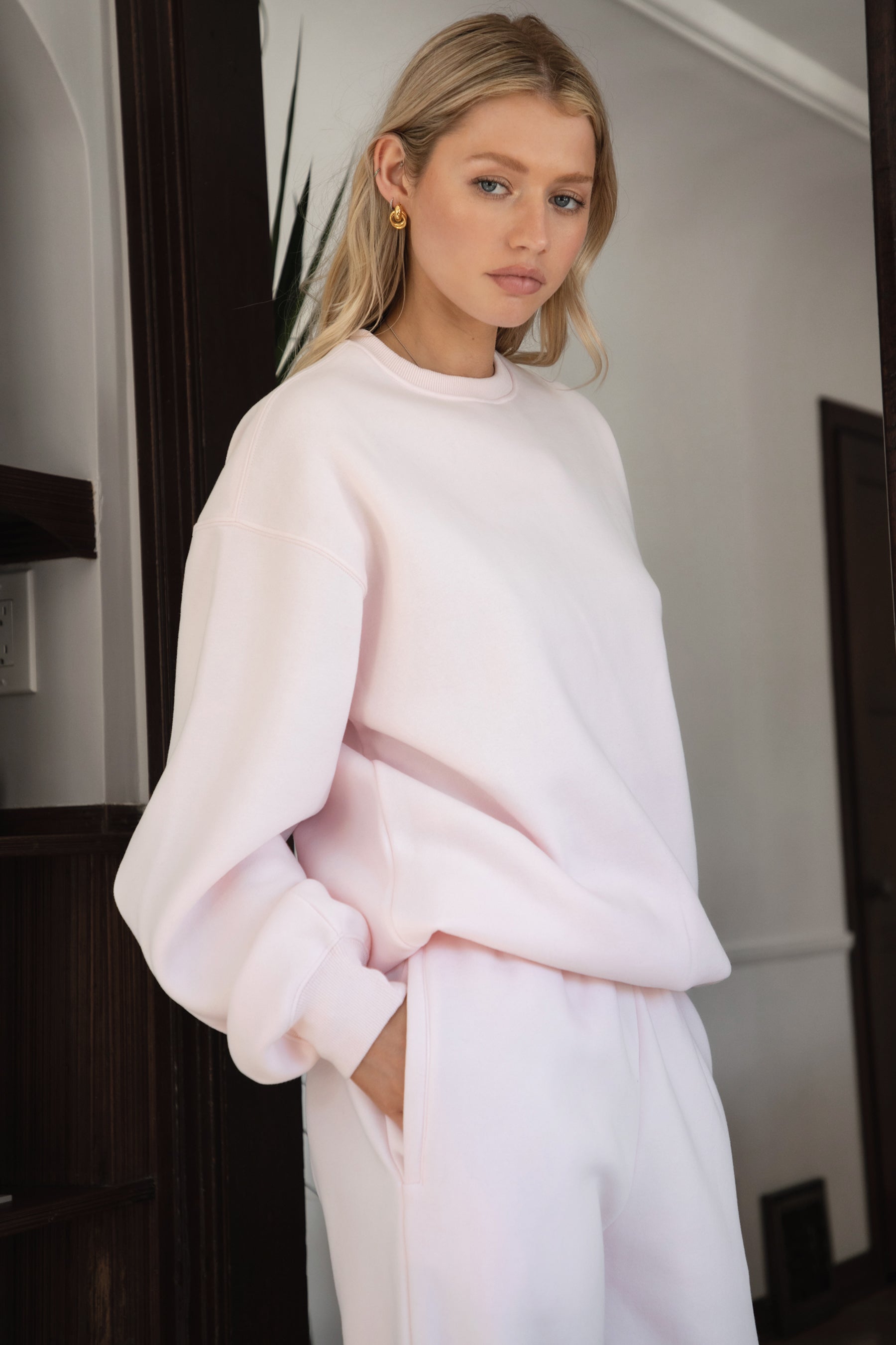 Woman wearing the TIC TOC TJ31656 LANI pale pink cloud fleece crew neck pullover sweatshirt featuring dropped shoulders, ribbed trim, and cozy fleece fabric with the matching bottoms indoors.