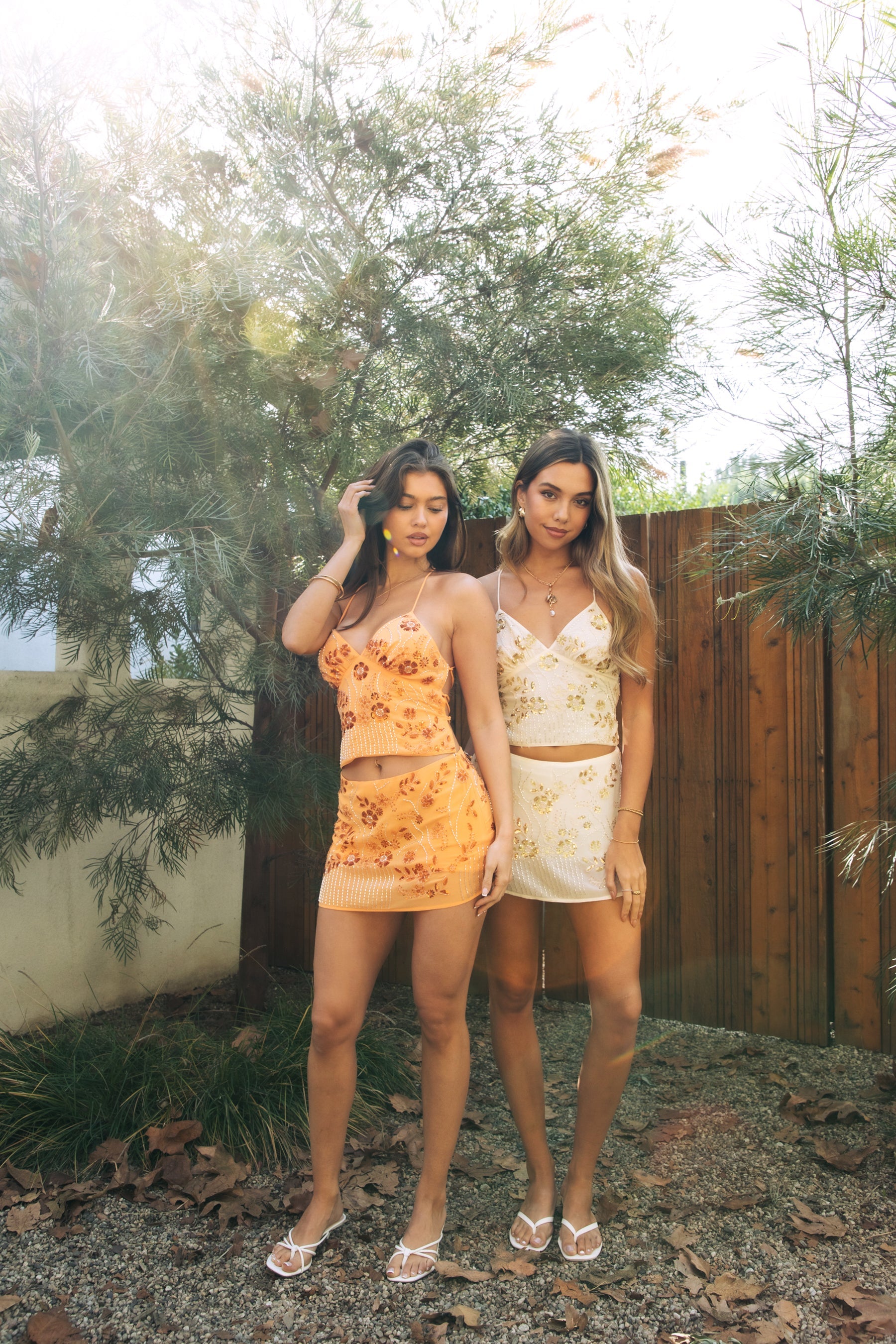 Model wearing the TIC TOC TL31430 VEDA brown chiffon beaded cami top featuring floral embroidery, plunging neckline, and lace-up open back with matching mini skirt in an outdoor setting