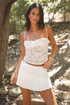 Woman wearing TIC TOC SH30319 EMMA low rise mini skort featuring a sexy pleated mini silhouette, built-in under shorts, bold pleats at the hem, and a low-rise waistband in a stretch denim-like fabric for a playful game day and back-to-school look.