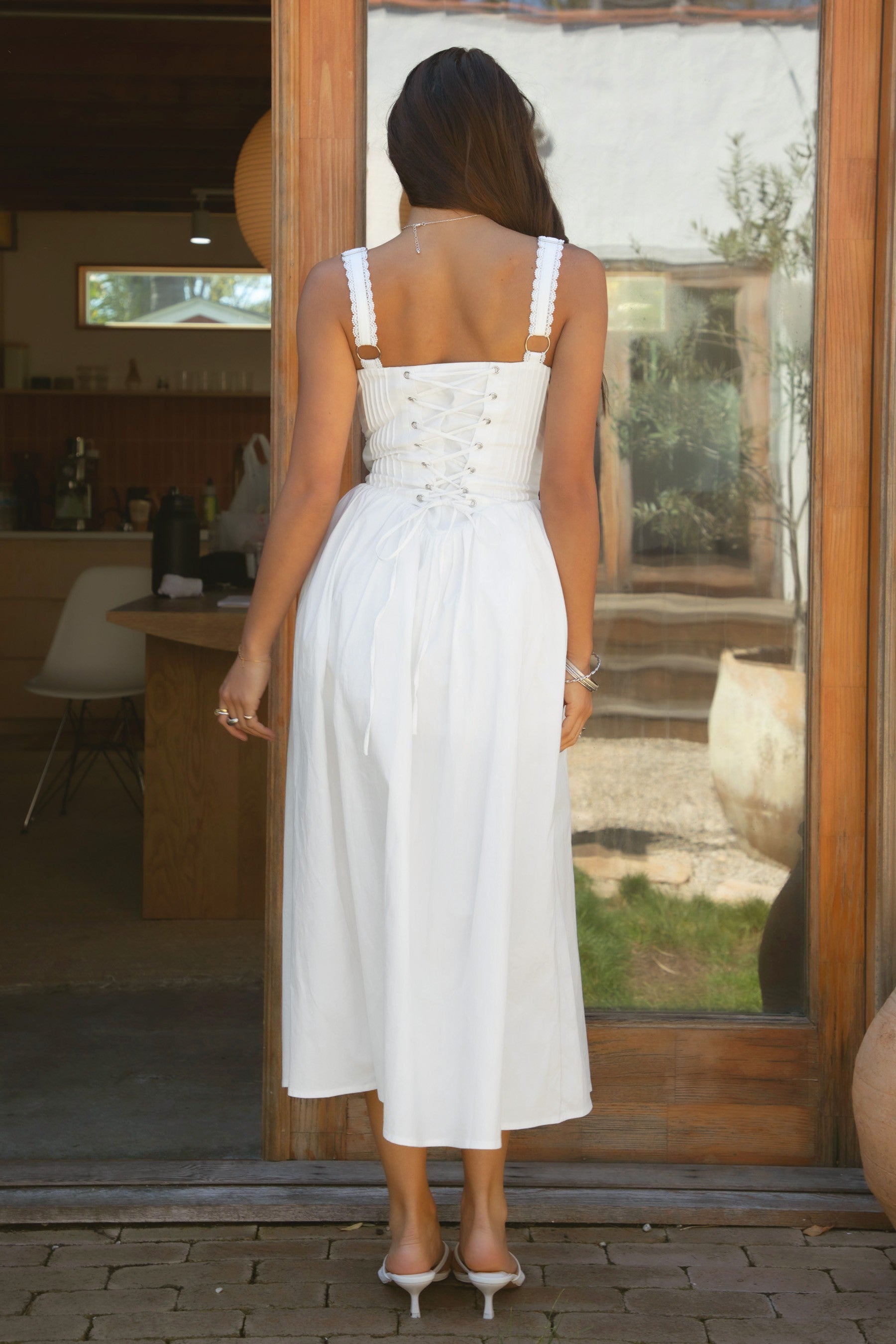 Woman wearing TIC TOC DA31086-LORETTA LORETTA stretch poplin maxi dress featuring adjustable lace shoulder straps, a cinched bust with bow detail, lace overlay corset-style bodice with vertical seaming, lace-up back and hidden side zipper, and a gathered A-line maxi skirt with a shaped waist and V-cut hip seam, styled for a romantic spring/summer occasion look.