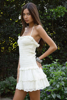 Woman wearing TIC TOC DA32031 ELLIE smocked body tiered ruffle lace halter mini dress featuring embroidered poplin fabric, a sculpted smocked bodice, halter neckline with self-tie strap, drop waist silhouette, and a tiered mini skirt with double layer eyelet lace hem for a romantic summer occasion look.