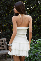 Woman wearing TIC TOC DA32031 ELLIE smocked body tiered ruffle lace halter mini dress featuring embroidered poplin fabric, a sculpted smocked bodice, halter neckline with self-tie strap, drop waist silhouette, and a tiered mini skirt with double layer eyelet lace hem for a romantic summer occasion look.