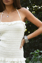 Woman wearing TIC TOC DA32031 ELLIE smocked body tiered ruffle lace halter mini dress featuring embroidered poplin fabric, a sculpted smocked bodice, halter neckline with self-tie strap, drop waist silhouette, and a tiered mini skirt with double layer eyelet lace hem for a romantic summer occasion look.