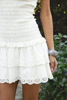 Woman wearing TIC TOC DA32031 ELLIE smocked body tiered ruffle lace halter mini dress featuring embroidered poplin fabric, a sculpted smocked bodice, halter neckline with self-tie strap, drop waist silhouette, and a tiered mini skirt with double layer eyelet lace hem for a romantic summer occasion look.