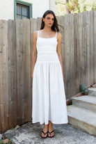 Woman wearing ISLA smocked poplin square neck maxi dress featuring smooth stretch poplin fabric, built in bra cups, straight neckline with ruffle detail, adjustable spaghetti straps, fully smocked bodice, flowing maxi skirt, hidden side pockets, and easy pull on design.