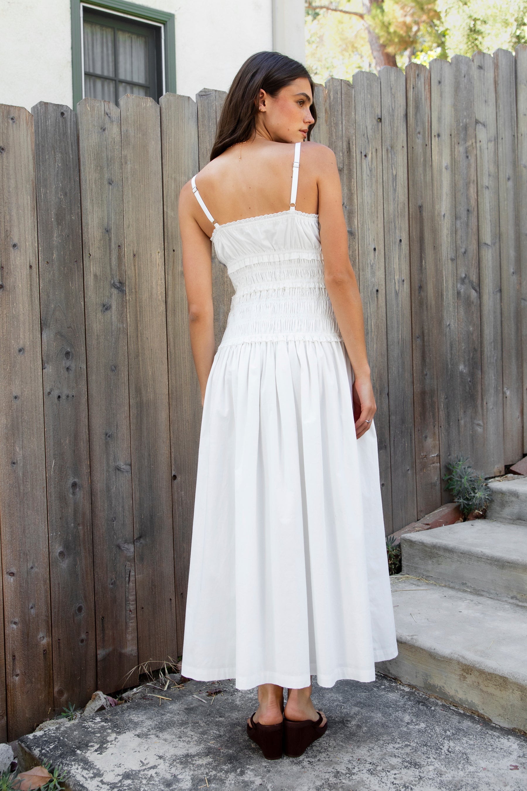 Woman wearing ISLA smocked poplin square neck maxi dress featuring smooth stretch poplin fabric, built in bra cups, straight neckline with ruffle detail, adjustable spaghetti straps, fully smocked bodice, flowing maxi skirt, hidden side pockets, and easy pull on design.
