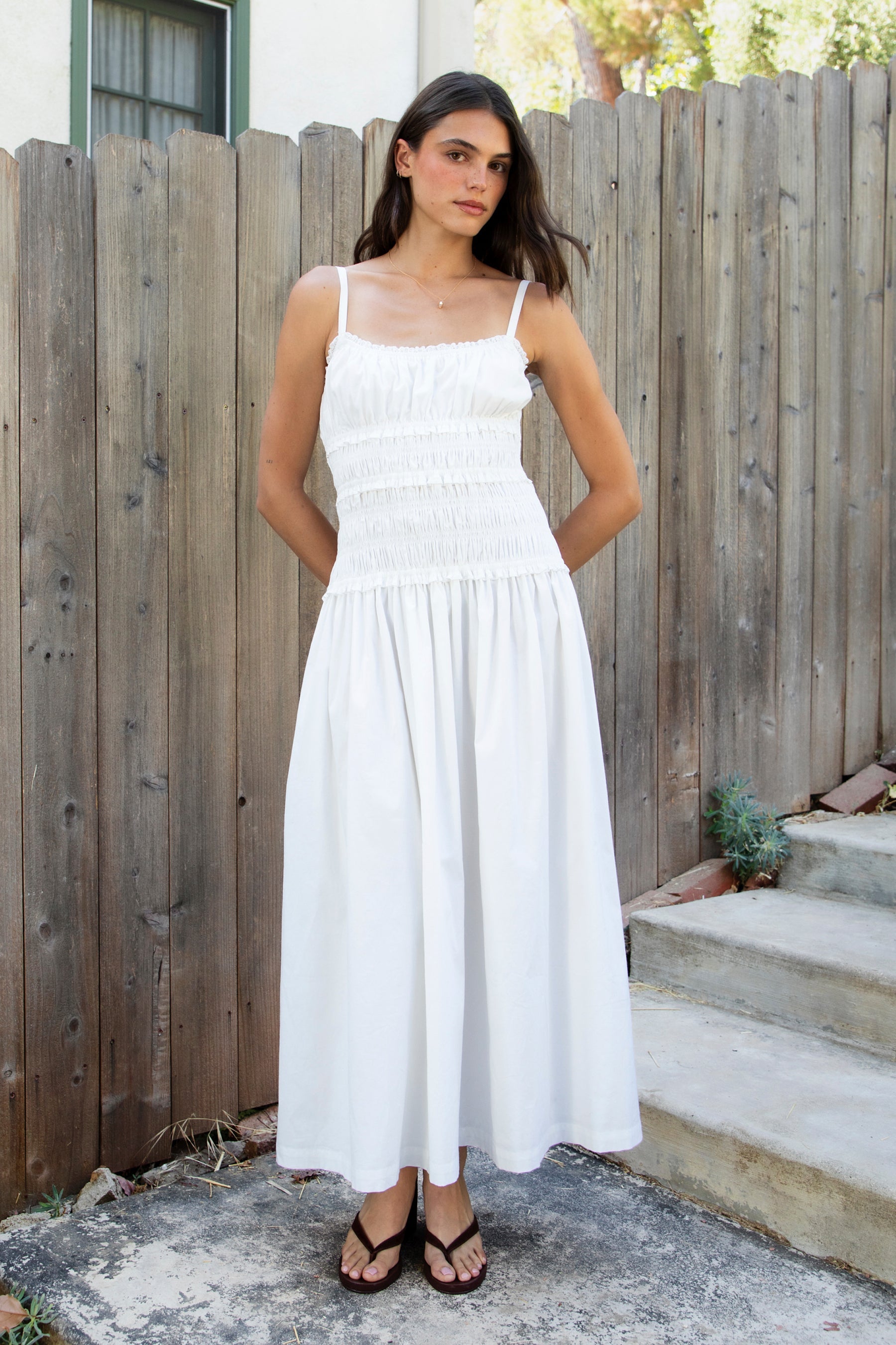 Woman wearing ISLA smocked poplin square neck maxi dress featuring smooth stretch poplin fabric, built in bra cups, straight neckline with ruffle detail, adjustable spaghetti straps, fully smocked bodice, flowing maxi skirt, hidden side pockets, and easy pull on design.