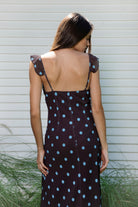 Woman wearing NOIRA ruffle chiffon polka dot maxi dress featuring flowy chiffon fabric, contrast polka dot print, deep V neckline with feminine ruffle trim, ruffled shoulder straps, adjustable front tie detail at the bust, fitted empire waist silhouette, low open back, adjustable shoulder straps, and soft stretch satin lining.