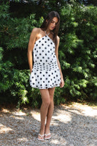 Woman wearing BIJOO polka dot chiffon halter mini dress featuring flowy chiffon fabric, bold polka dot print, adjustable self tie halter neckline, open back silhouette, relaxed blouson bodice, ruched waistband detailing, layered flared mini skirt, and fully lined construction for comfortable coverage.