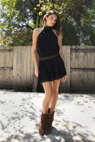 Woman wearing VESPER studded chiffon halter mini dress featuring flowy chiffon fabric, soft feminine drape, high halter neckline with self tie back closure, open back silhouette, gold studded geometric detailing along the neckline and waist, blouson bodice, gathered details, flared mini skirt, sheer chiffon overlay, and full lining.