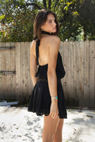 Woman wearing VESPER studded chiffon halter mini dress featuring flowy chiffon fabric, soft feminine drape, high halter neckline with self tie back closure, open back silhouette, gold studded geometric detailing along the neckline and waist, blouson bodice, gathered details, flared mini skirt, sheer chiffon overlay, and full lining.