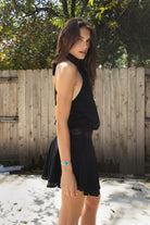 Woman wearing VESPER studded chiffon halter mini dress featuring flowy chiffon fabric, soft feminine drape, high halter neckline with self tie back closure, open back silhouette, gold studded geometric detailing along the neckline and waist, blouson bodice, gathered details, flared mini skirt, sheer chiffon overlay, and full lining.