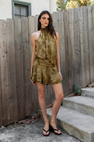 Woman wearing OLIVINE flocked sleeveless floral halter ruched mini dress featuring soft flocked jersey fabric, stretch jersey lining, smocked high halter neckline, open back design, ruched drop waist, layered flounce mini skirt, and pull on construction for special occasion styling.