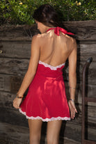 Women wearing TIC TOC CHERRIE Polka Dot Halter Mini Dress in red with plunging V neckline, lace trim hem, and open back design paired with western frye brown boots in front of a wooden wall. 