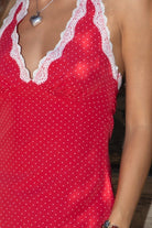 Women wearing TIC TOC CHERRIE Polka Dot Halter Mini Dress in red with plunging V neckline, lace trim hem, and open back design paired with western frye brown boots in front of a wooden wall. 