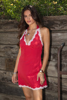 Women wearing TIC TOC CHERRIE Polka Dot Halter Mini Dress in red with plunging V neckline, lace trim hem, and open back design paired with western frye brown boots in front of a wooden wall. 