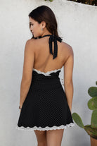 Woman wearing a black polka dot dress with lace trim against a light gray background