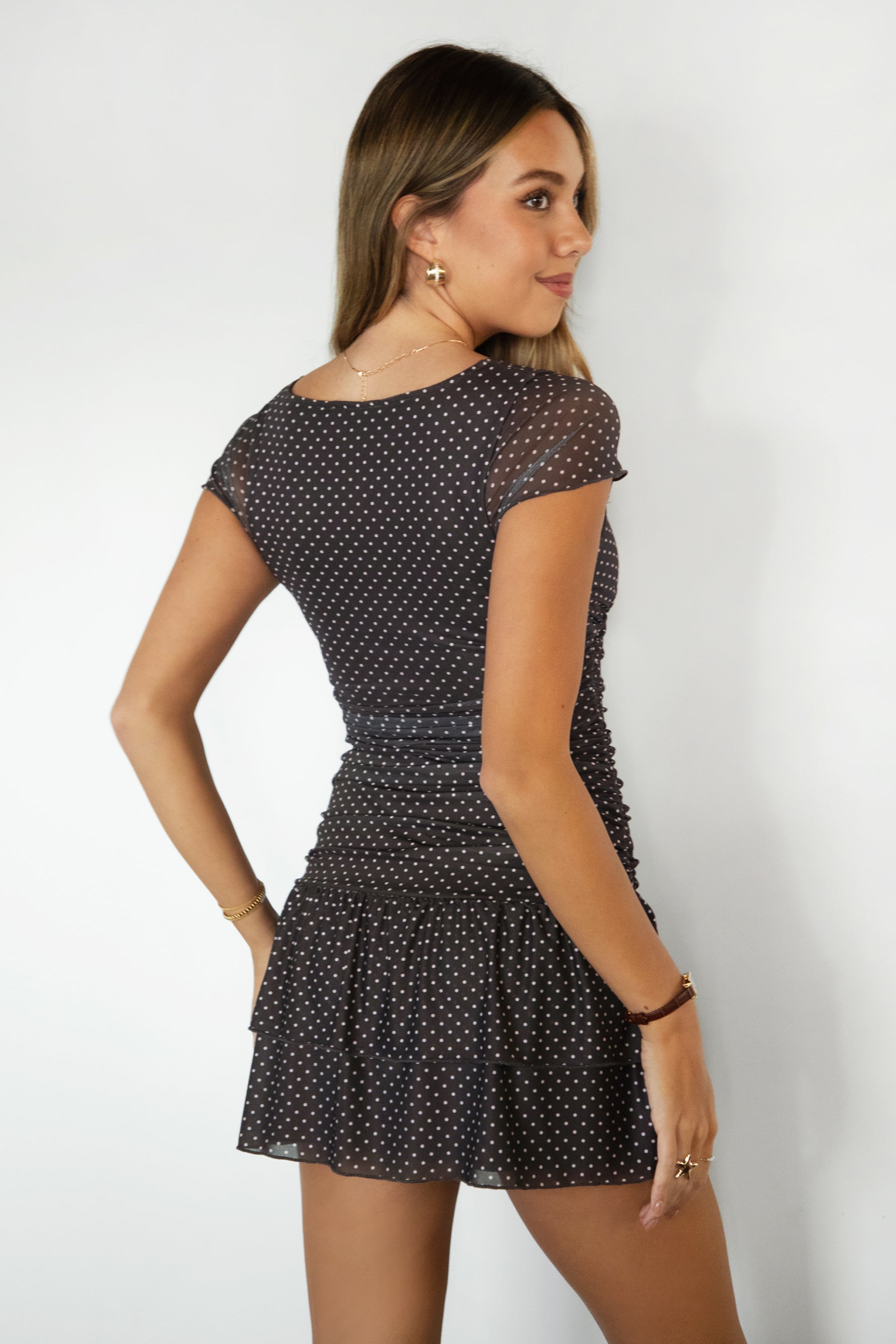 Woman wearing TIC TOC DC32004-ALOURA ALOURA micro polka dot deep V-neck mini dress featuring a plunging V-neckline with center mini bow detail, floaty sheer mesh cap sleeves, ruched fitted mesh body with micro polka dot overlay, tiered ruffle mini skirt hem, and lightweight sheer mesh construction, styled with heels for a flirty going-out look.