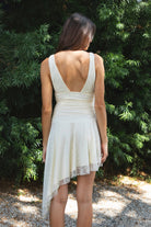 Woman wearing FIORA flocked dot asymmetrical mini dress featuring soft flocked dot mesh, sleeveless silhouette, deep V neckline with gathered bust detail, ruched fitted waist, low V back neckline, asymmetrical handkerchief hem with extended side drape, and soft interlock jersey lining.