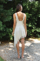 Woman wearing FIORA flocked dot asymmetrical mini dress featuring soft flocked dot mesh, sleeveless silhouette, deep V neckline with gathered bust detail, ruched fitted waist, low V back neckline, asymmetrical handkerchief hem with extended side drape, and soft interlock jersey lining.