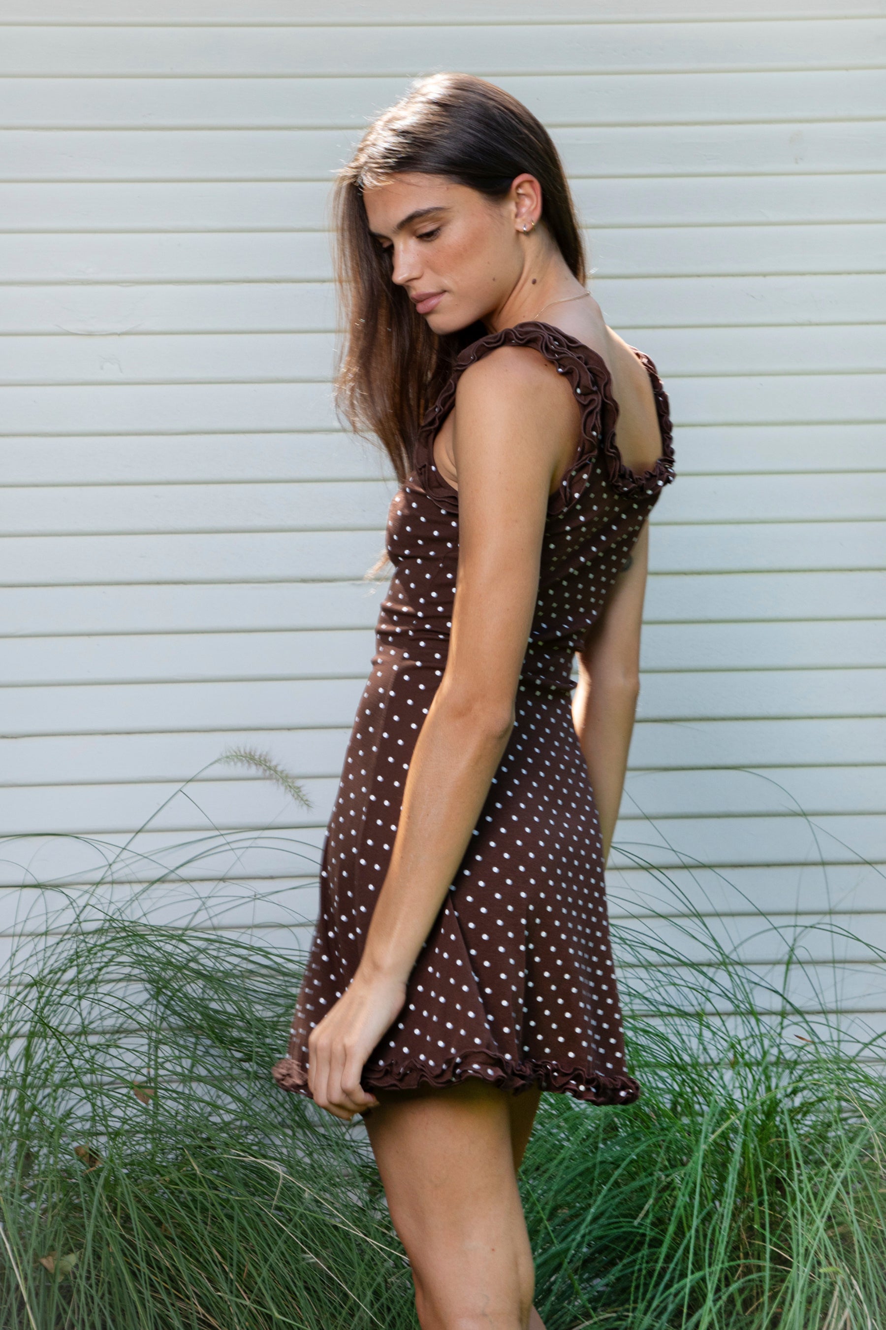 Woman wearing MOXI ruffle polka dot stretch mini dress featuring soft stretch cotton jersey fabric, allover polka dot print, scoop neckline with layered ruffle trim, wide ruffled shoulder straps, fitted bodice, softly flared skirt, and double ruffle trim along the mini hem.