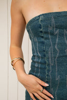 Woman wearing ARIZONA denim western stitch mini dress featuring vintage washed denim, bold western inspired contrast stitching, strapless corset style bodice, lace up back with adjustable closure, subtle back cutout, fitted waist, and a soft stretch mini length silhouette.